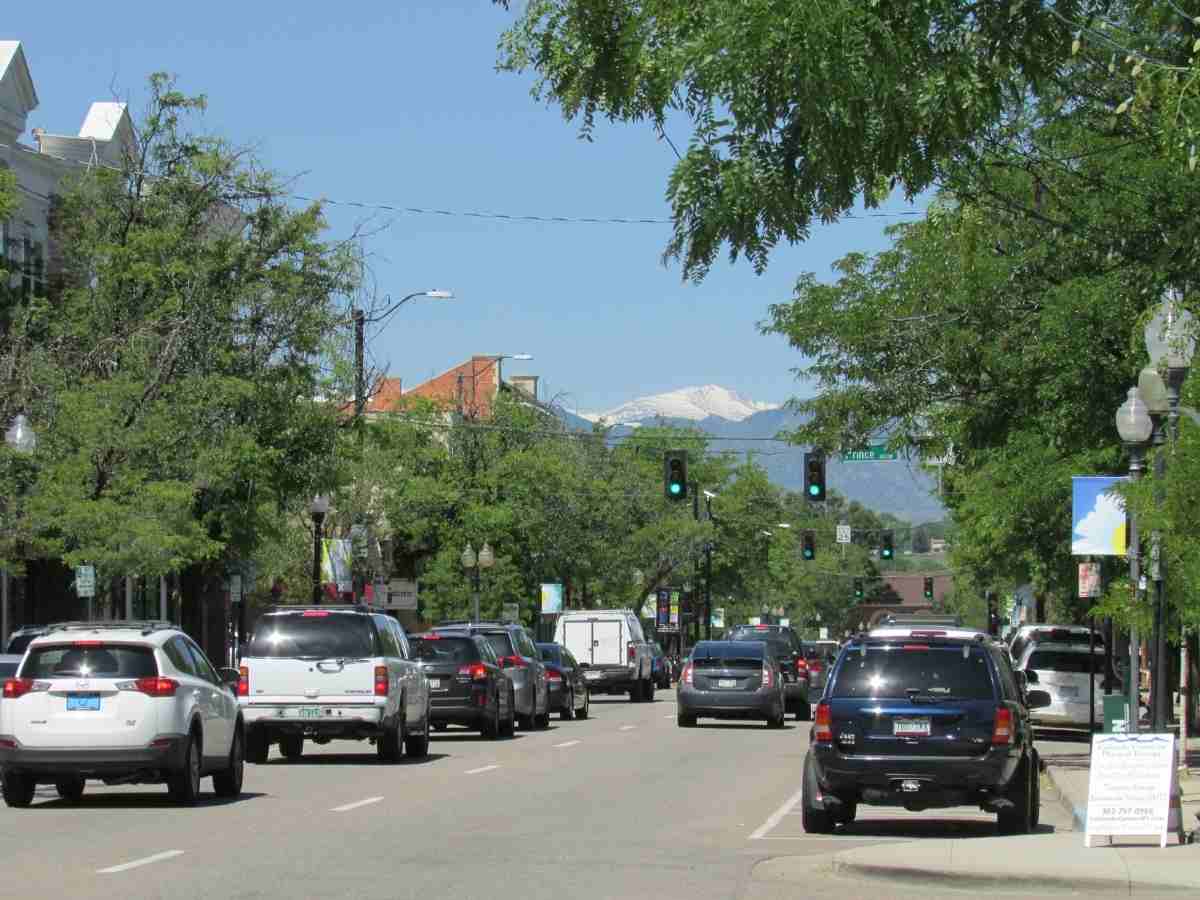 Road with cars and trees on side with mountains in the background for article Littleton Colorado for newcomers moving to Denver area.