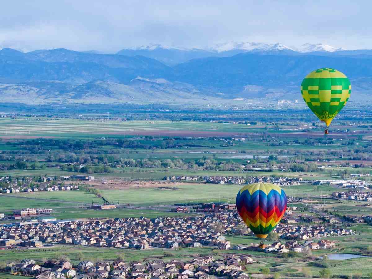 Aerial View of neighborhoods with 2 hot air balloons flying above them and mountains in the background for article Erie Colorado for newcomers moving to Denver area.