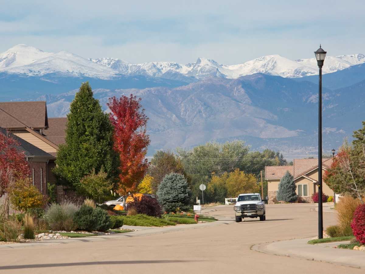 Neighborhood in fall showing street with a truck parked on it, colorful trees on the side of the road and houses on the edge with mountains in the background for article Firestone Colorado for newcomers moving to Denver area.