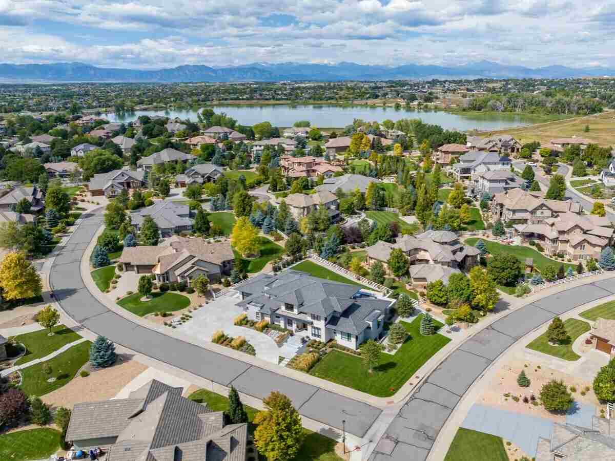 Aerial view of Lexington Shores subdivision with large homes a lake beyond the homes, and the mountains in the distance for article Westminster Colorado for newcomers moving to the Denver area.