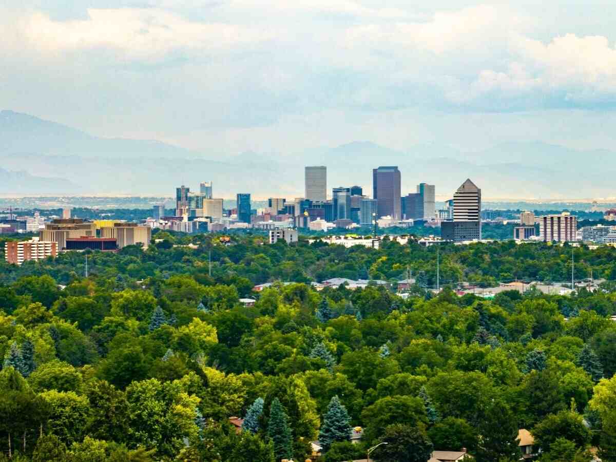 Aerial view showing the city of Denver far off in the background and lots of trees in the foreground for article Top 25 Suburban Communities Surrounding Denver for newcomers moving to Denver suburbs.