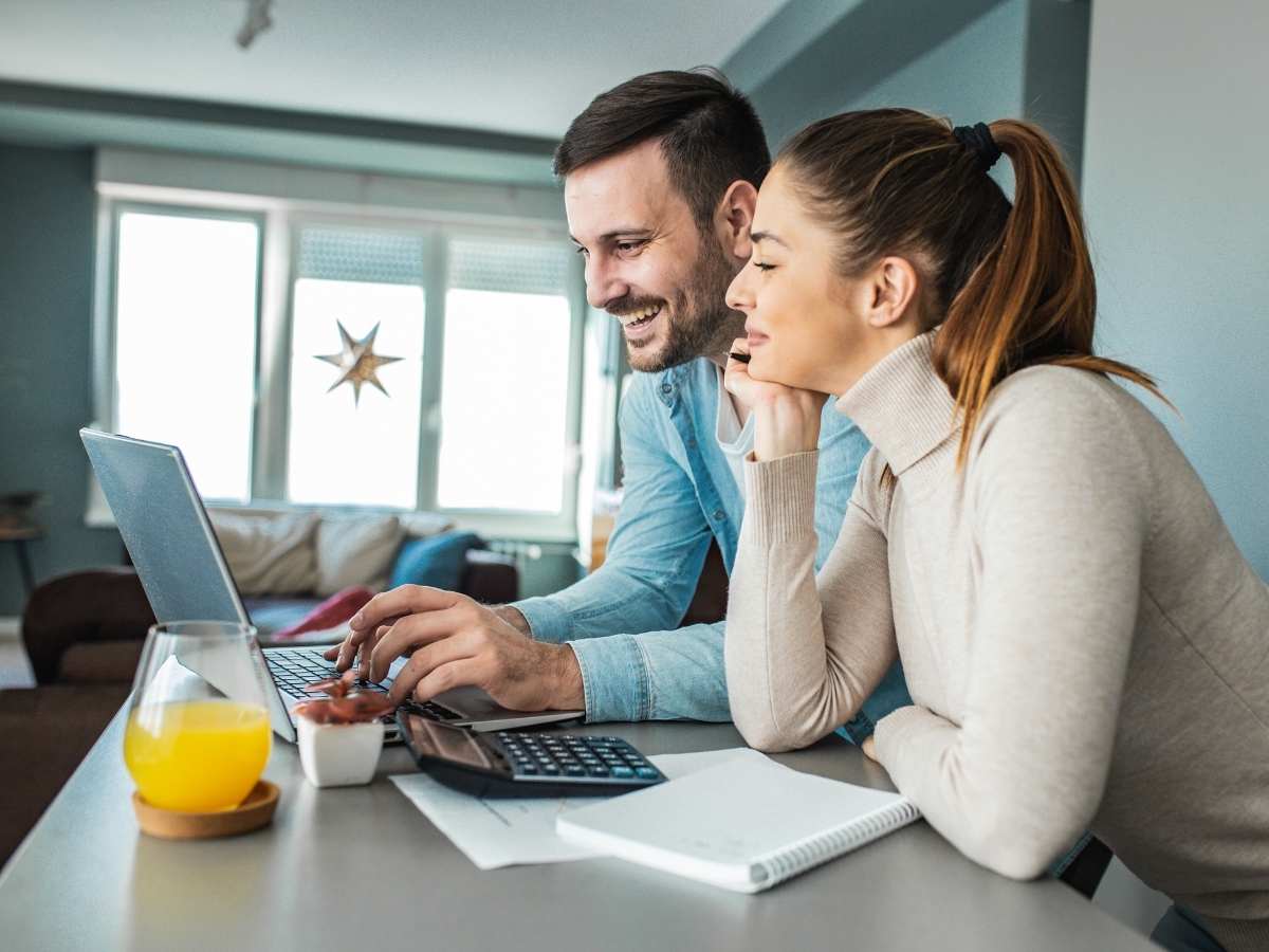 Young millennial couple looking at laptop with papers and calculator for article Millennials buying homes in Denver for newcomers moving to Denver area.