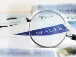 magnifying glass over papers highlighting the word wages for article Minimum Wage in Colorado for newcomers moving to Denver area.