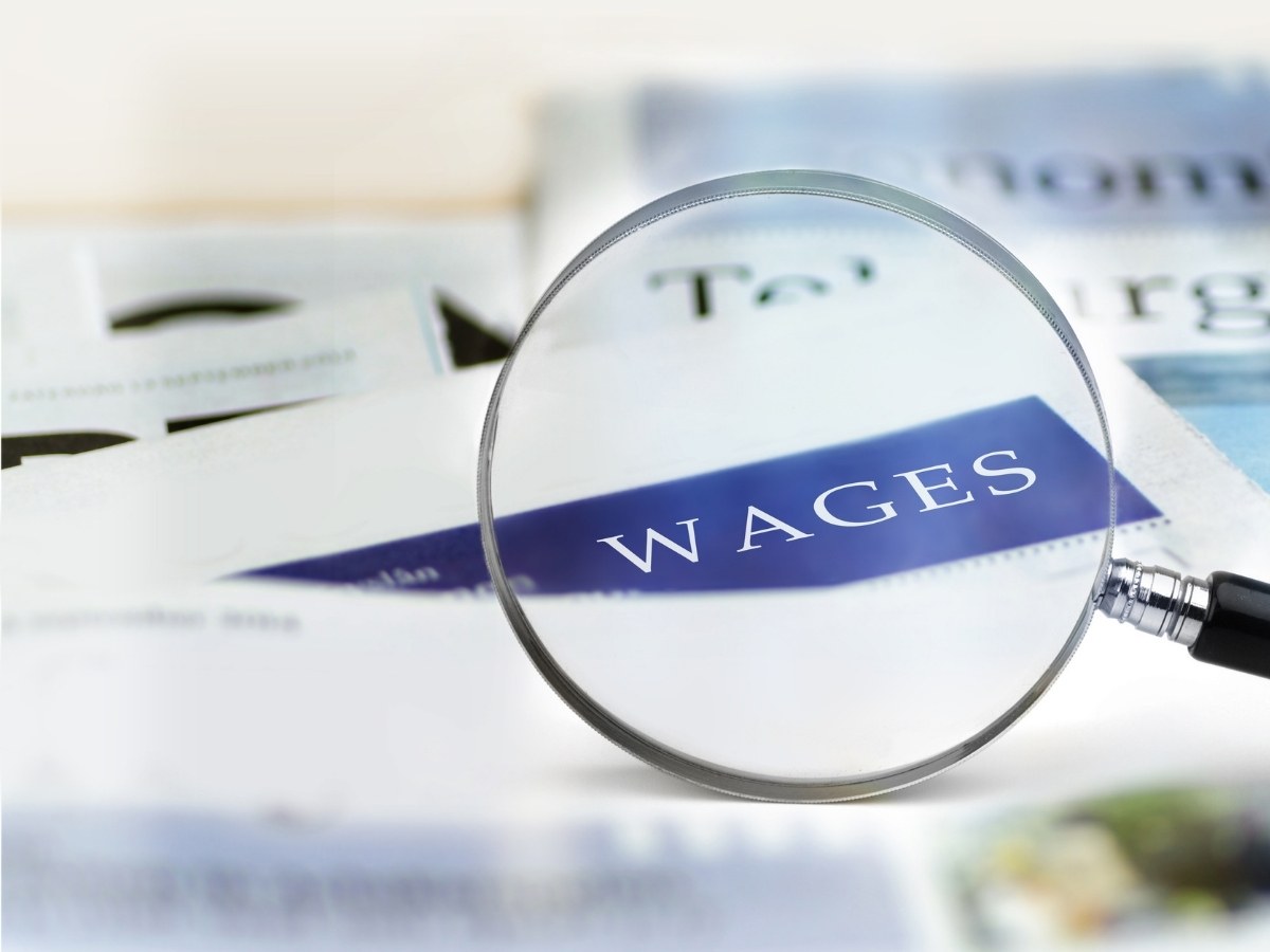 magnifying glass over papers highlighting the word wages for article Minimum Wage in Colorado for newcomers moving to Denver area.