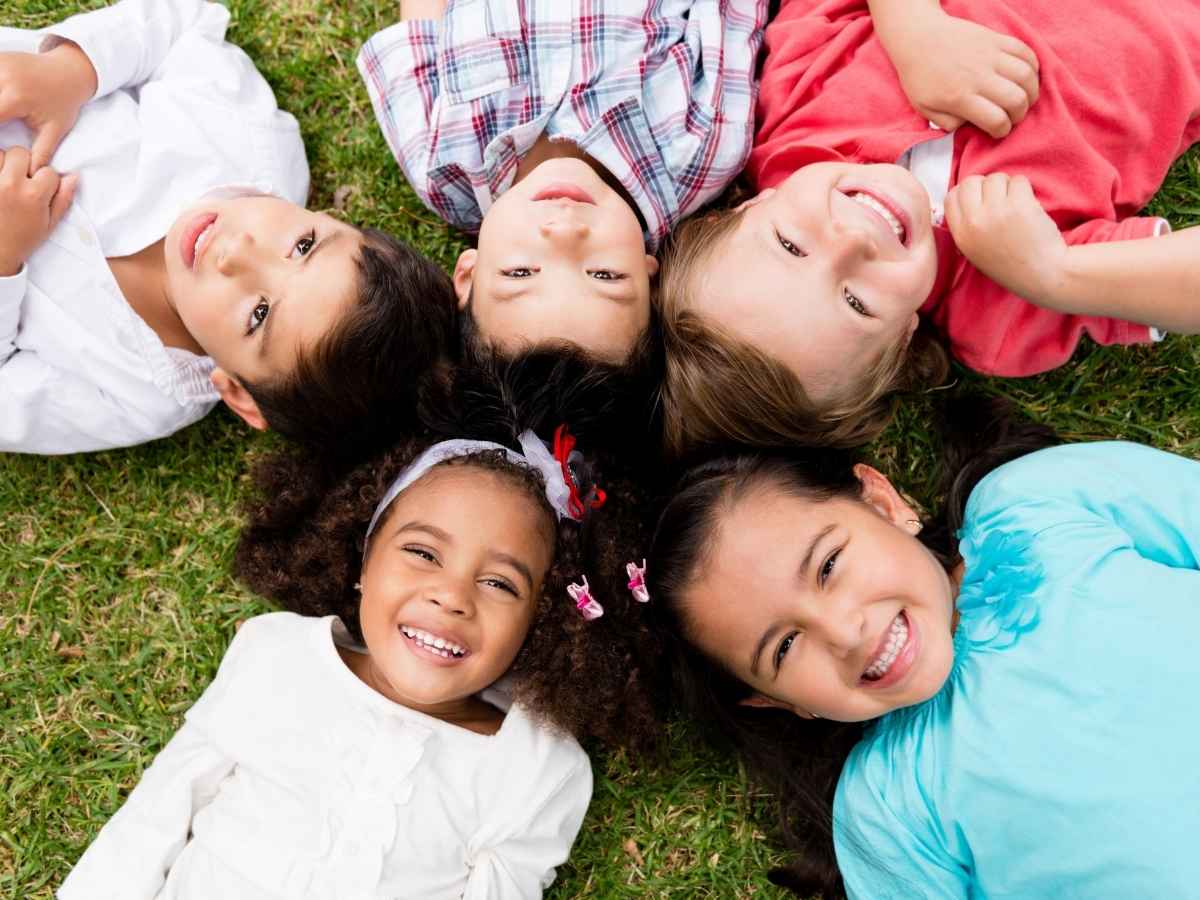 kids laying on ground in a circle with heads in center looking up at cameral and smiling for article Parenting Advice in Denver for newcomers moving to Denver area.