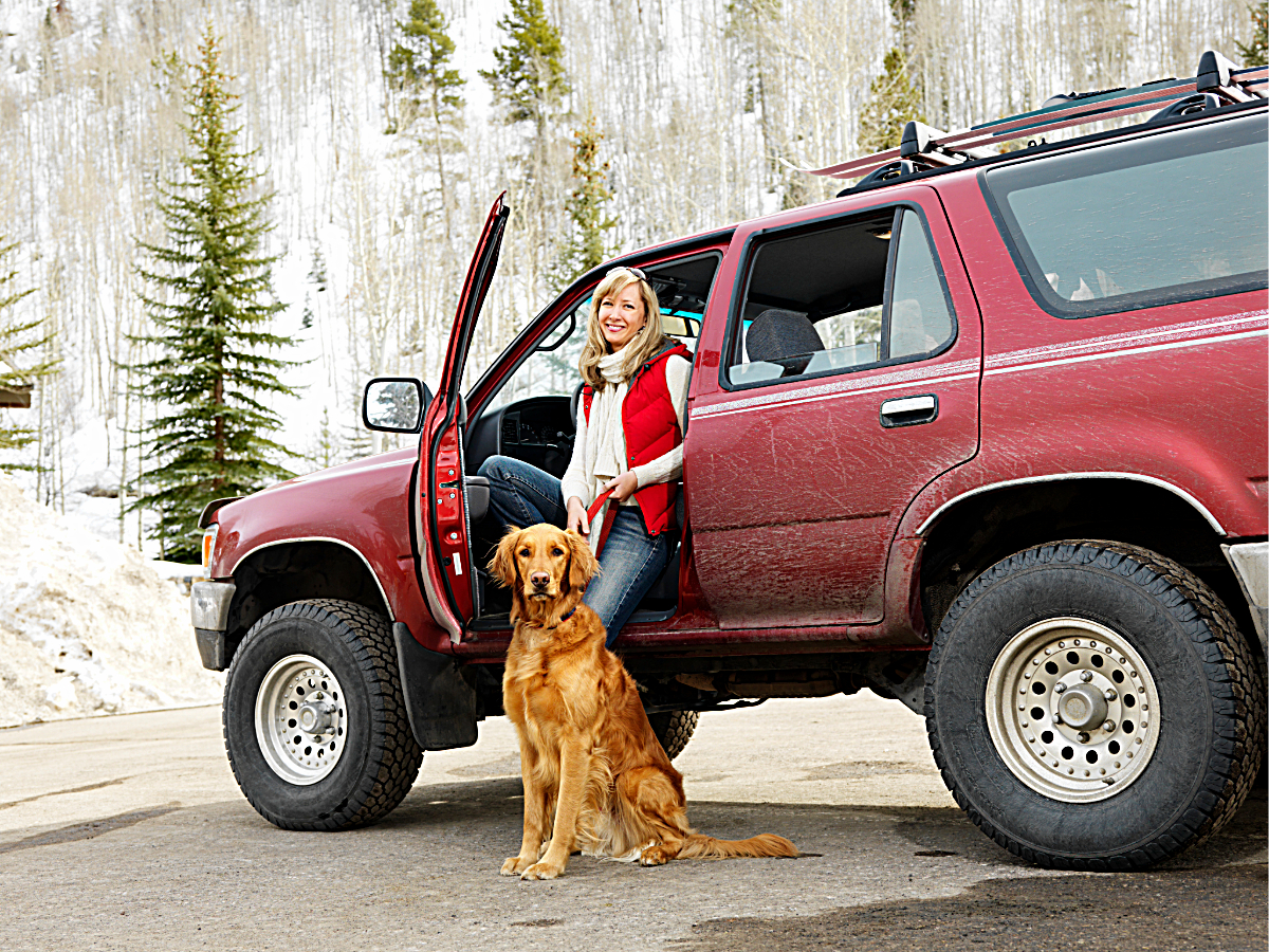 Woman standing in front of Red SUV with the door open and dog sitting at her feet for article What to Drive When Moving to Colorado for newcomers moving to Denver.