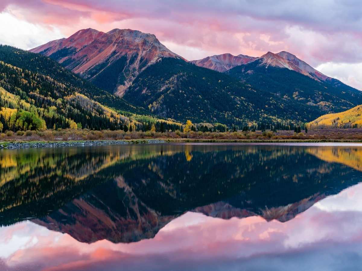 Colorado Mountains in the background with a pick and gray sky and all being reflected in a lake in the foreground for article 4 Cities Named Best Places to Live in Colorado for newcomers moving to Colorado.