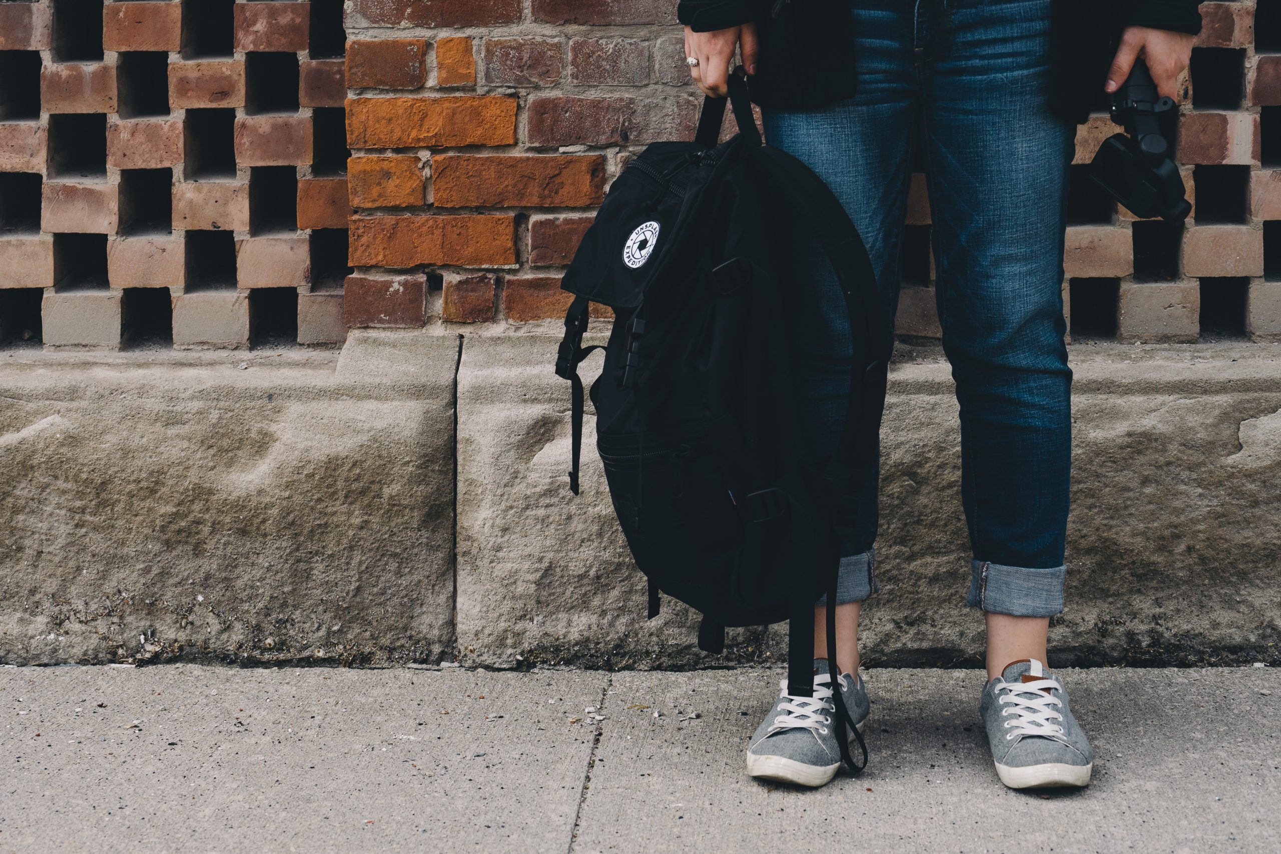 A person holding a backpack and standing on a sidewalk for article Top 20 Private High Schools in Colorado for newcomers moving to Colorado.