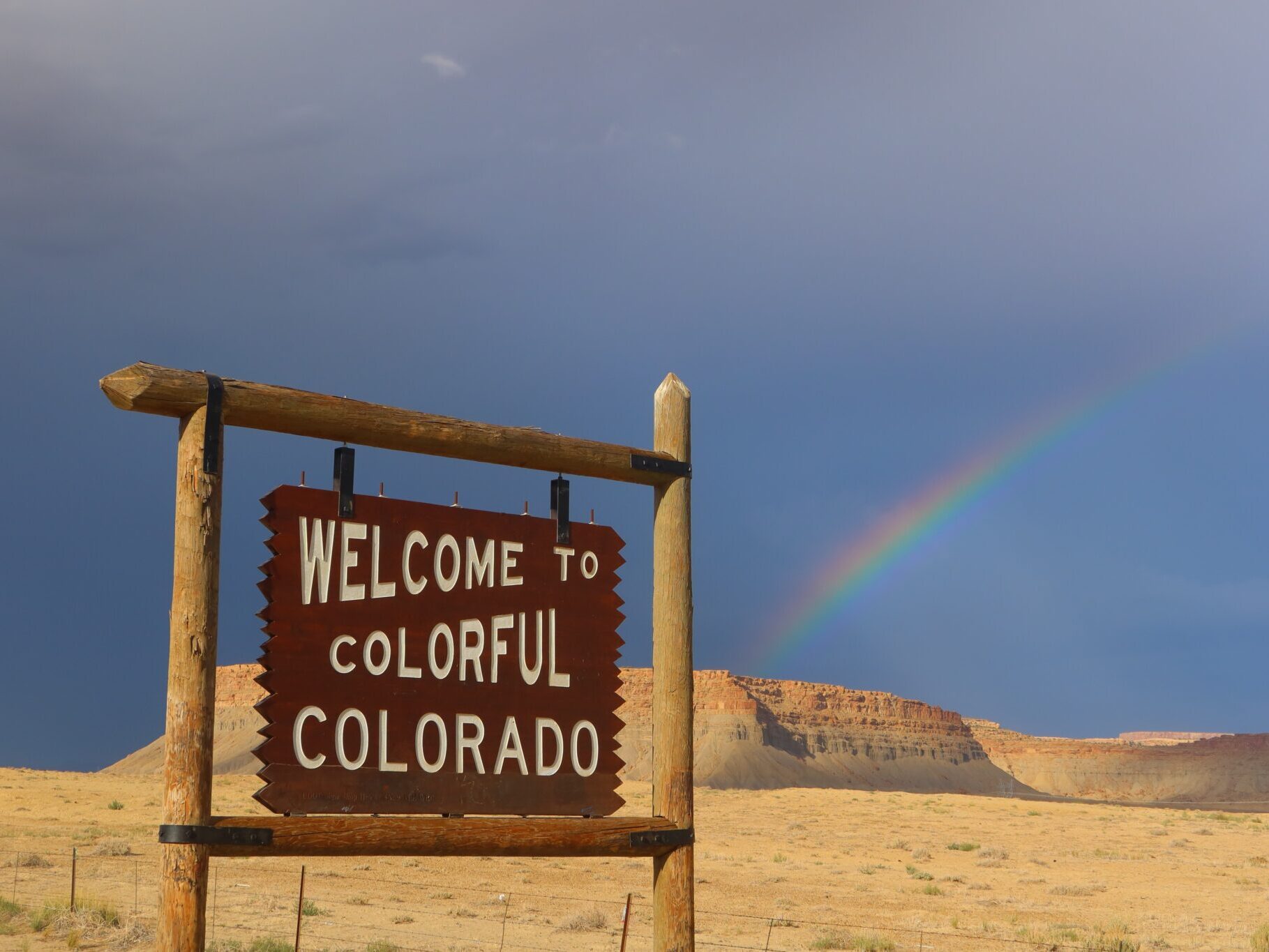 "welcome to colorful colorado" wooden sign with blue sky and rainbow in the background