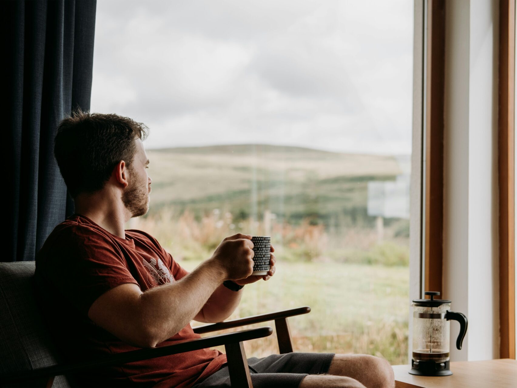 man looking outside in mountain home, holding cup