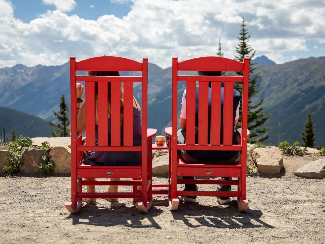 2 People Sitting in Red Adirondack Chairs facing the mountains