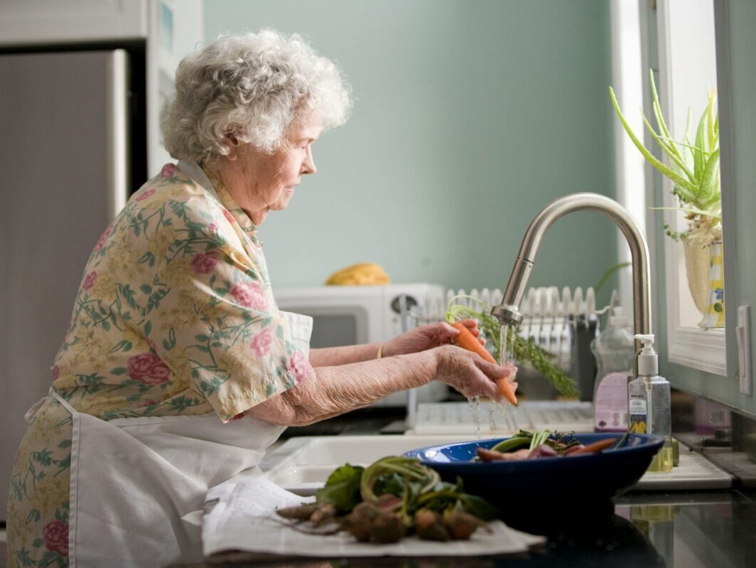 elderly woman washing carrots in the sink in a kithcen