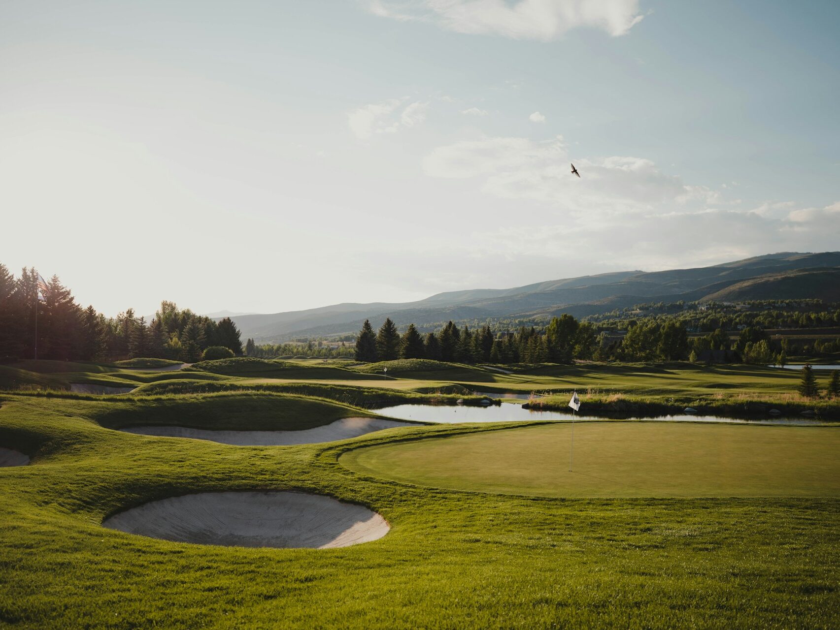 elongated view of a golf course green with mountains in the distance on a sunny day