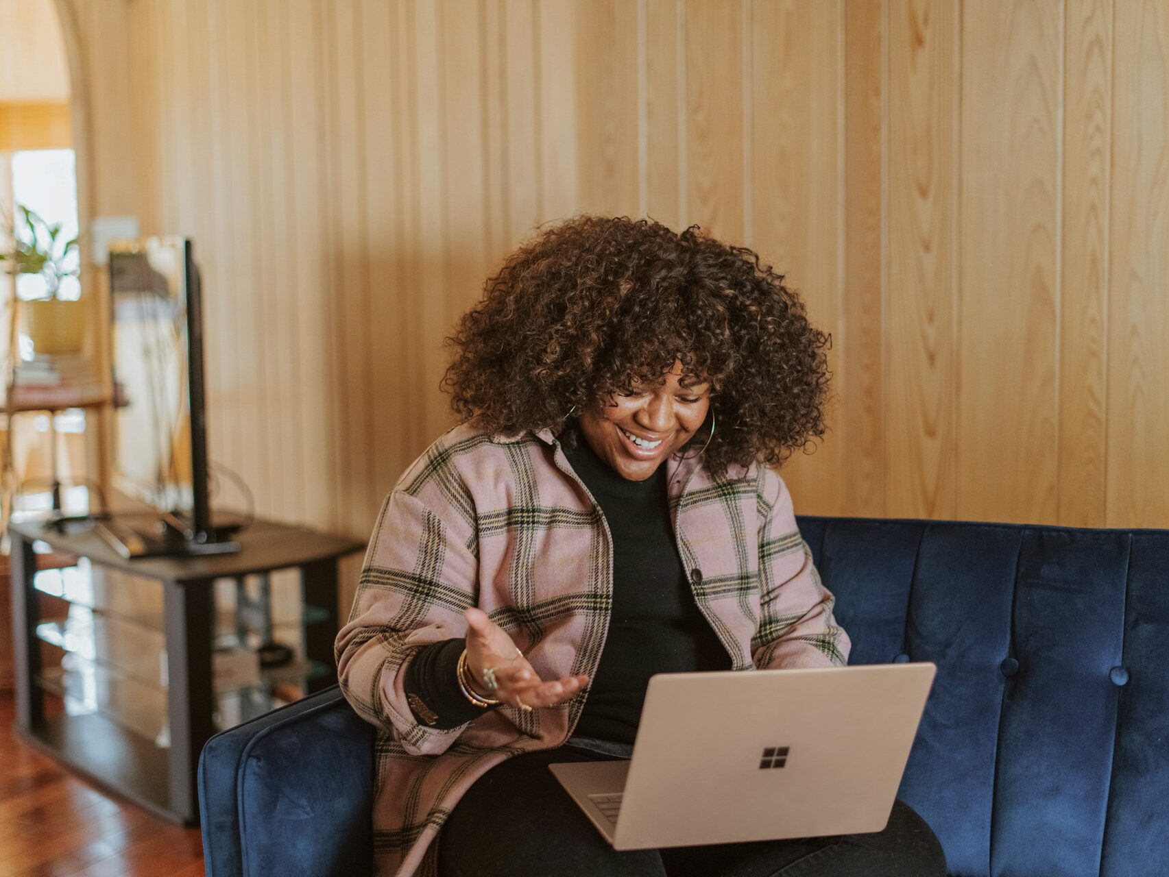 woman sitting on a blue couch speaking and laughing while working on her laptop