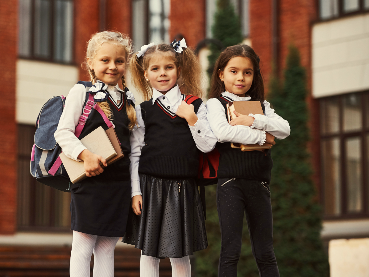 3 Girls in school uniforms posing in front of school.