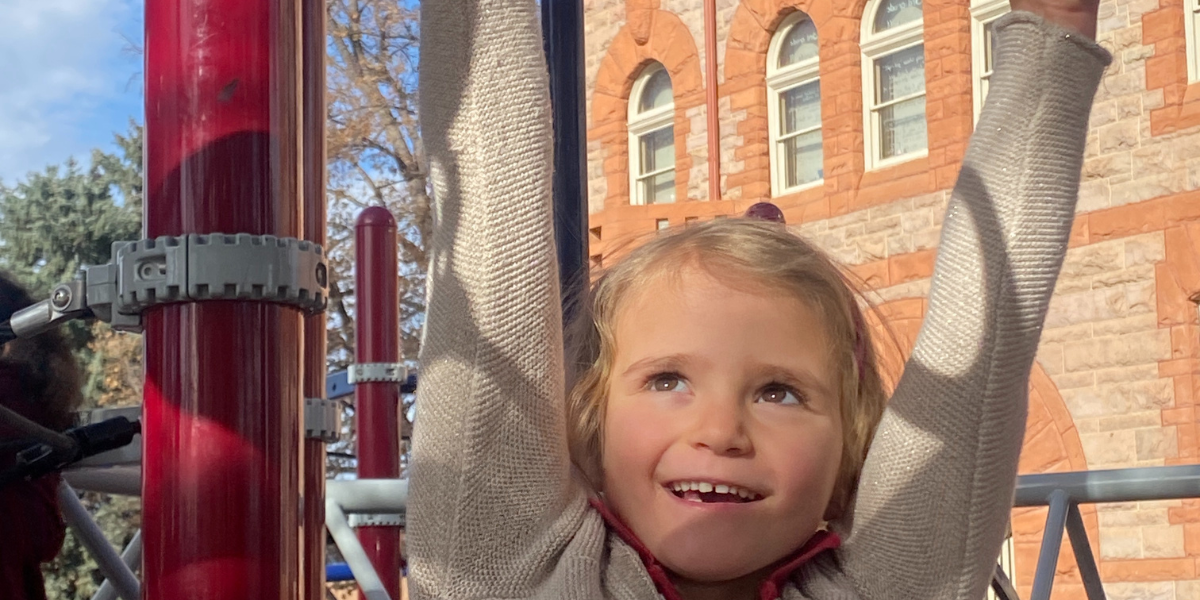 young blonde stuent hanging from monkey bars in front of St. Elizabeth's School