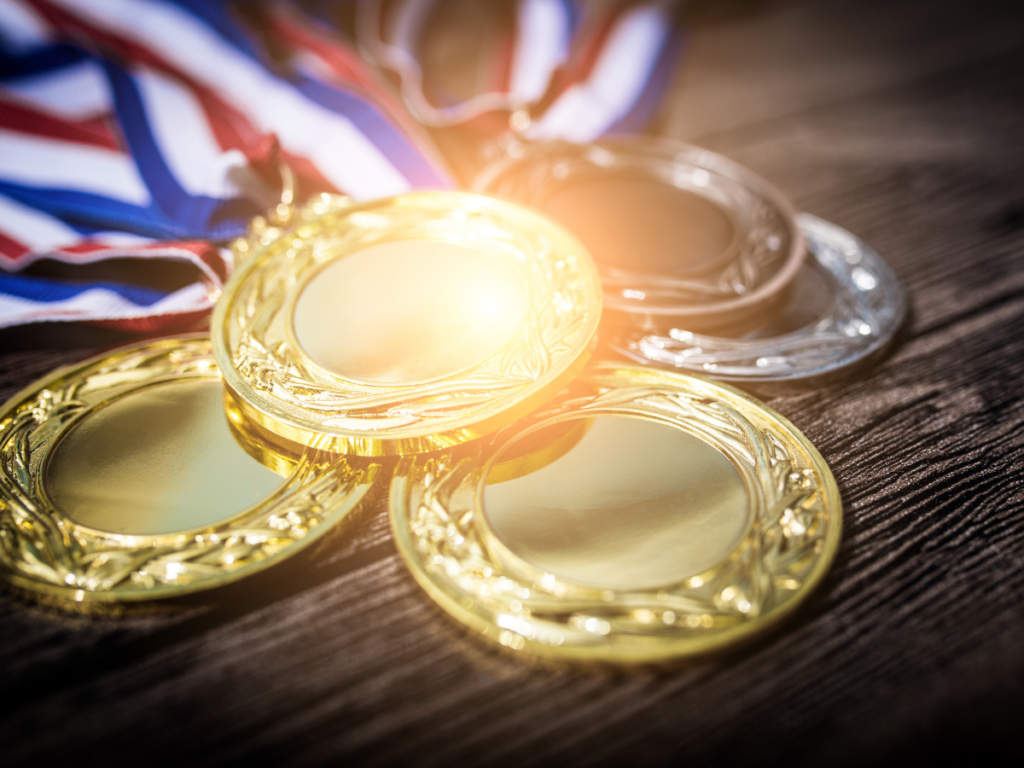 1st, 2nd, 3rd place medals stacked on table with red, white and blue ribbons attached.