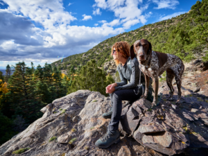 Woman and her dog sitting on rocky area in Colorado outside of Denver for article on Denver being a city for Dog Lovers for newcomers moving to Denver.