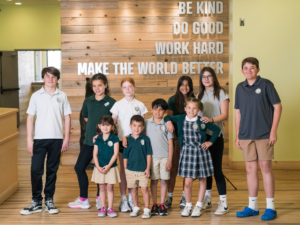 Aspen Academy kids of all ages k-8 standing in front of wall with Be Kind, Do Good, Work Hard, and Make the World A Better Place on it.