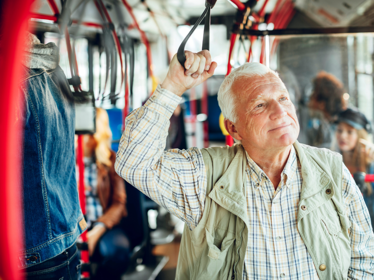 Senior man holding onto strap on bus ride.