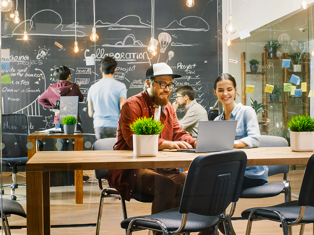 Coworking startup space with people collaborating and big chalkboard with ideas.