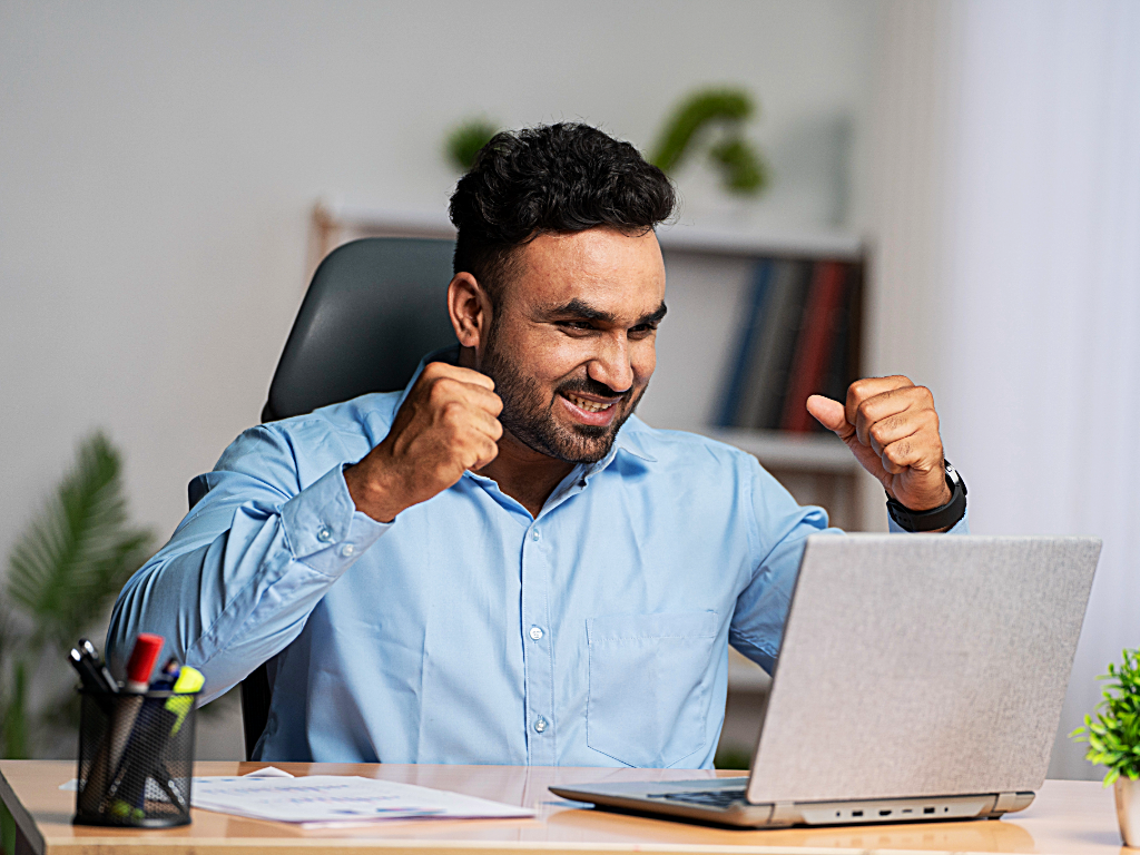 Person celebrating in front of computer after finding contract work online.