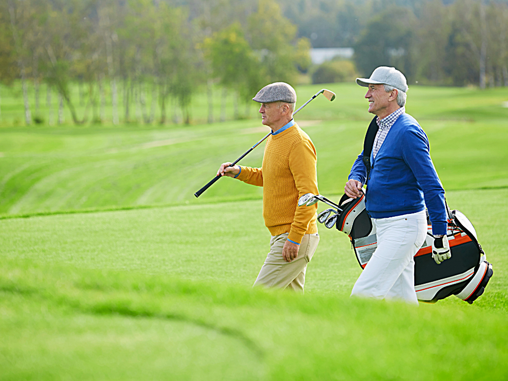 2 men walking side by side on hilly golf course. 1 is carrying golf club over shoulder, the other is carrying golf bag for article on golf courses in Denver.