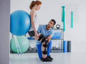 Physical therapist guiding client with a knee brace on with Bosu ball assisted wall squats.