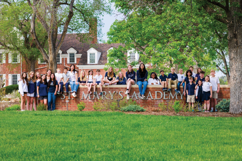 Group of kids sitting outside St. Mary's School brick entrance wall for article - St. Mary’s Academy Educating Denver since 1864 for newcomers moving to Denver.