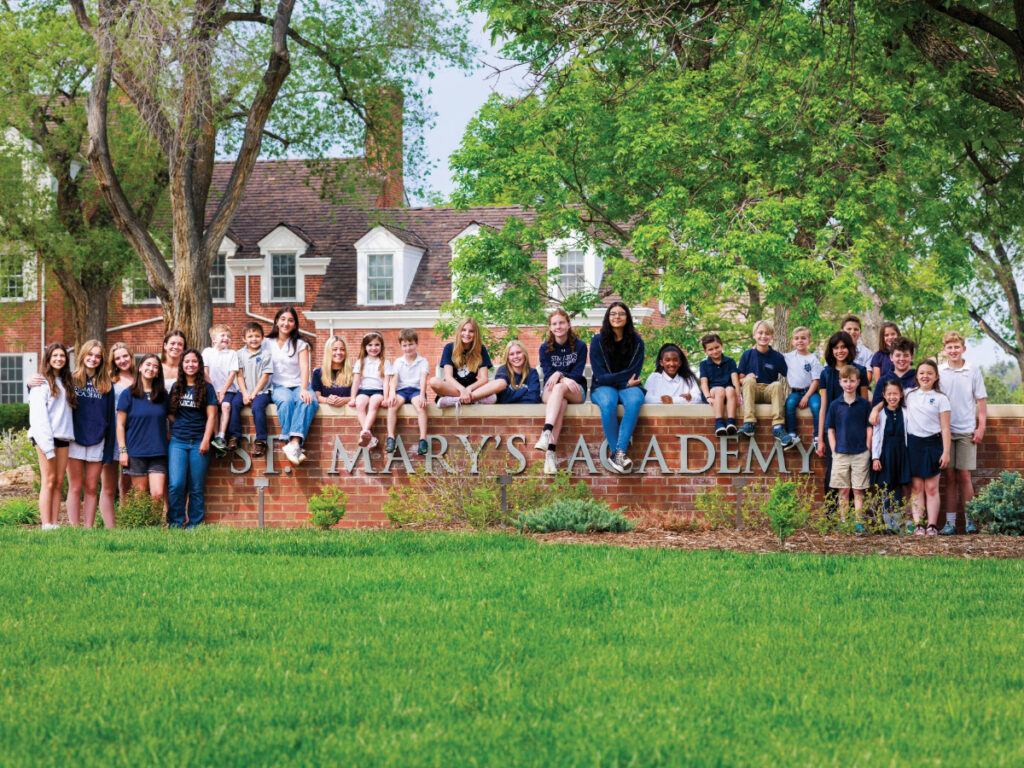 Group of kids sitting outside St. Mary's School brick entrance wall for article St. Mary's Academy Educating Denver since 1864 for newcomers moving to Denver.