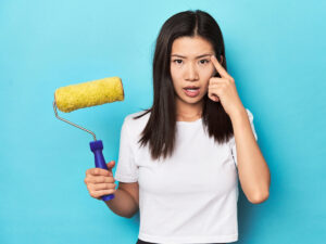 Woman holding paint roller with whoops look on her face for article 7 Costly Painting Mistakes to Avoid for newcomers moving to Denver.