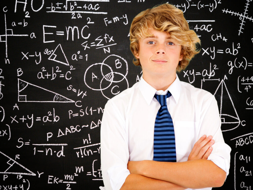 High school boy in private school uniform with arms crossed in front of chalkboard with math equations all over it for article Top 4 Private High Schools in Denver for newcomers moving to Denver.