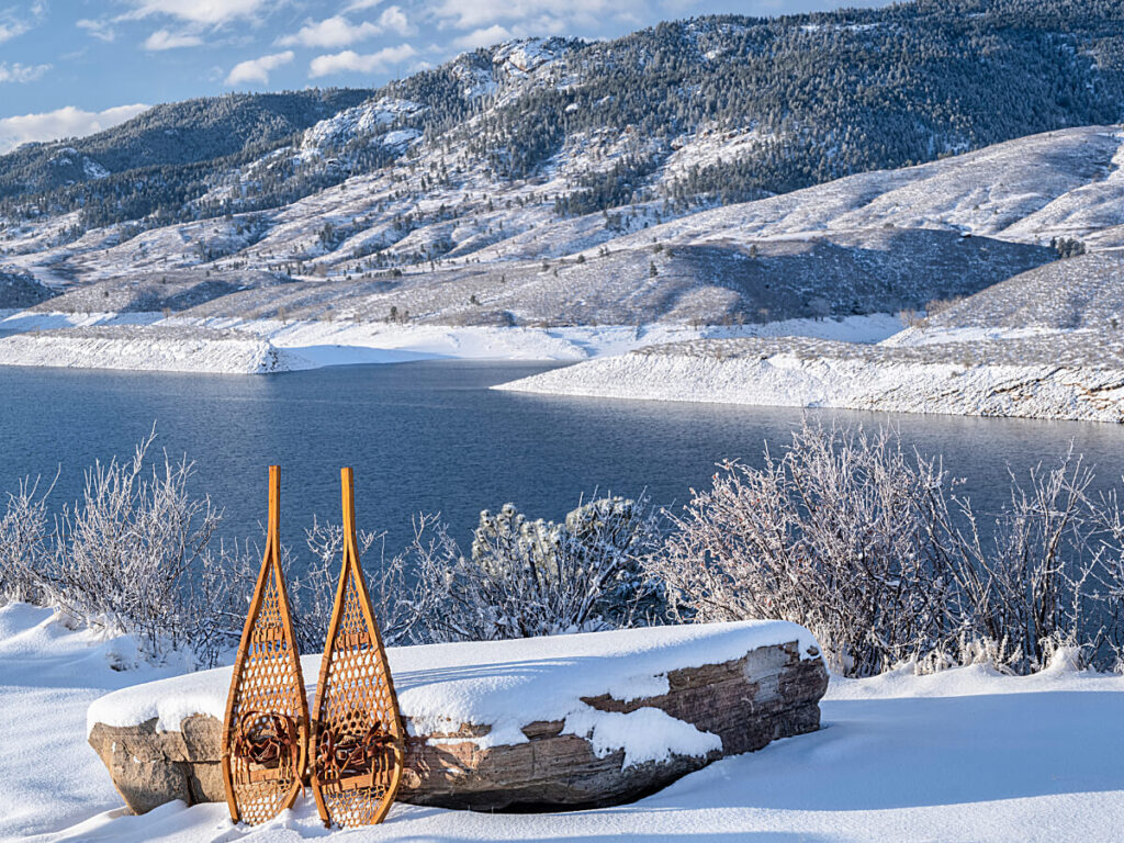 Scenic view of northern Colorado with mountains in the background and a lake and snowshoes leaning on a rock in the foreground for article Exploring Northern Colorado: A Prime Destination for Newcomers moving to Colorado