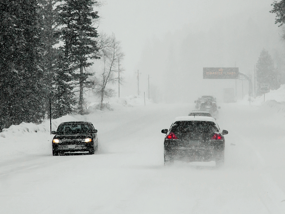 Cars driving on both sides of the road in very snowy conditions on Colorado roads for article Winter Driving in Colorado for newcomers moving to Denver.