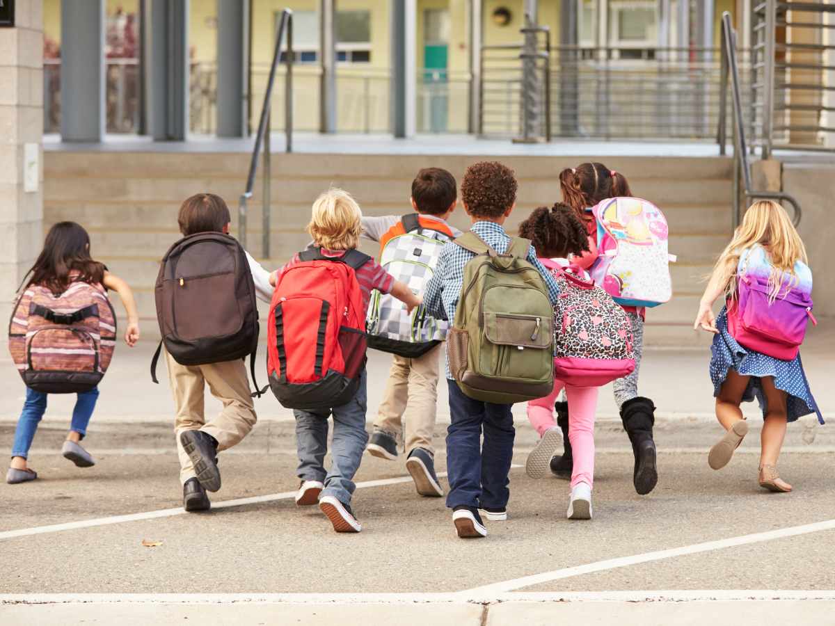 8 kids with large backpacks on running toward steps of public school for article Top Public Elementary Schools In Denver for newcomers moving to Denver.