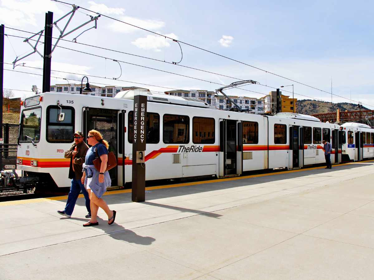 man and woman walking on sidewalk in front of light rail train for article Score Big with Easy Transit: Take the Train to Your Favorite Denver Events for newcomers moving to Denver.