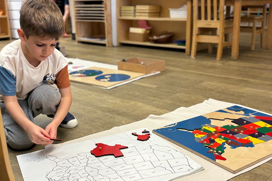 Boy working on puzzle of the United States laying the state shapes on the map on the ground for article Montessori Academy of Colorado for newcomers moving to Denver.