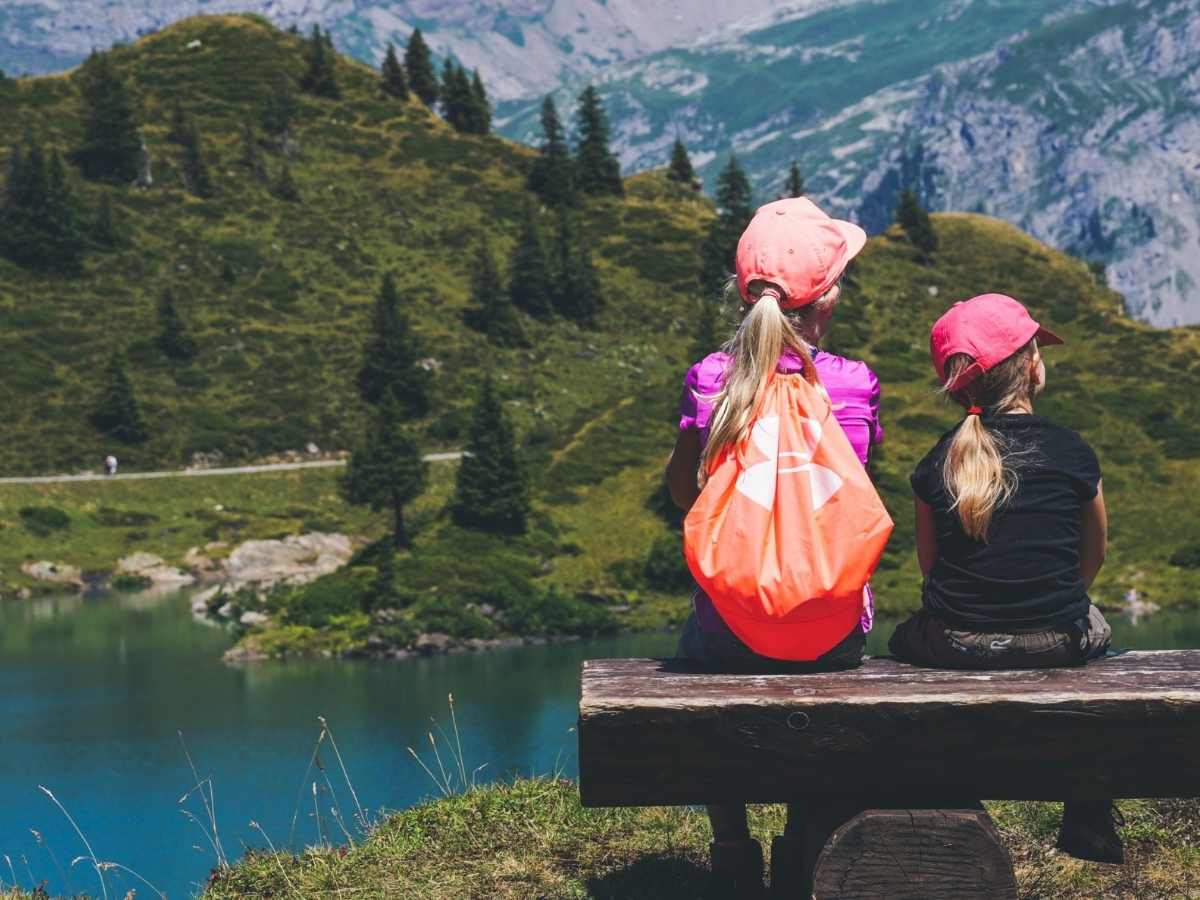 2 Girls sitting on a wood bench looking out over a lake and Colorado mountains for article Summer Camps in Colorado for newcomers moving to Denver.