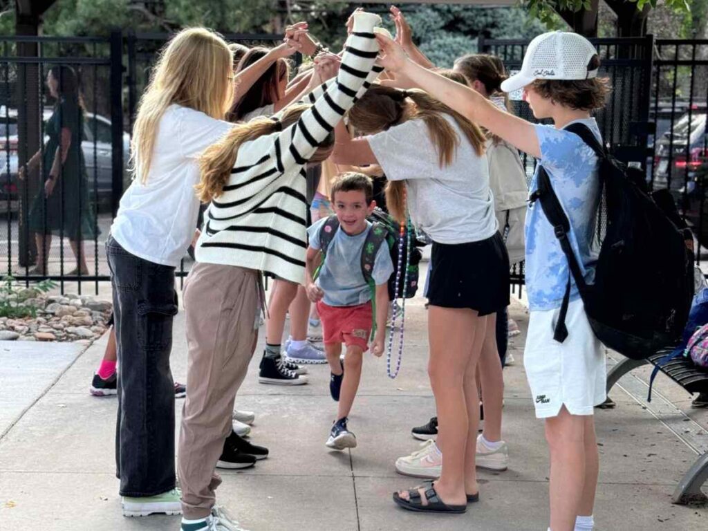 Small child running through an arch of arms held high by older students for article The Joy Factor: How Montessori School of Denver Helps Kids Thrive for newcomers moving to Denver.