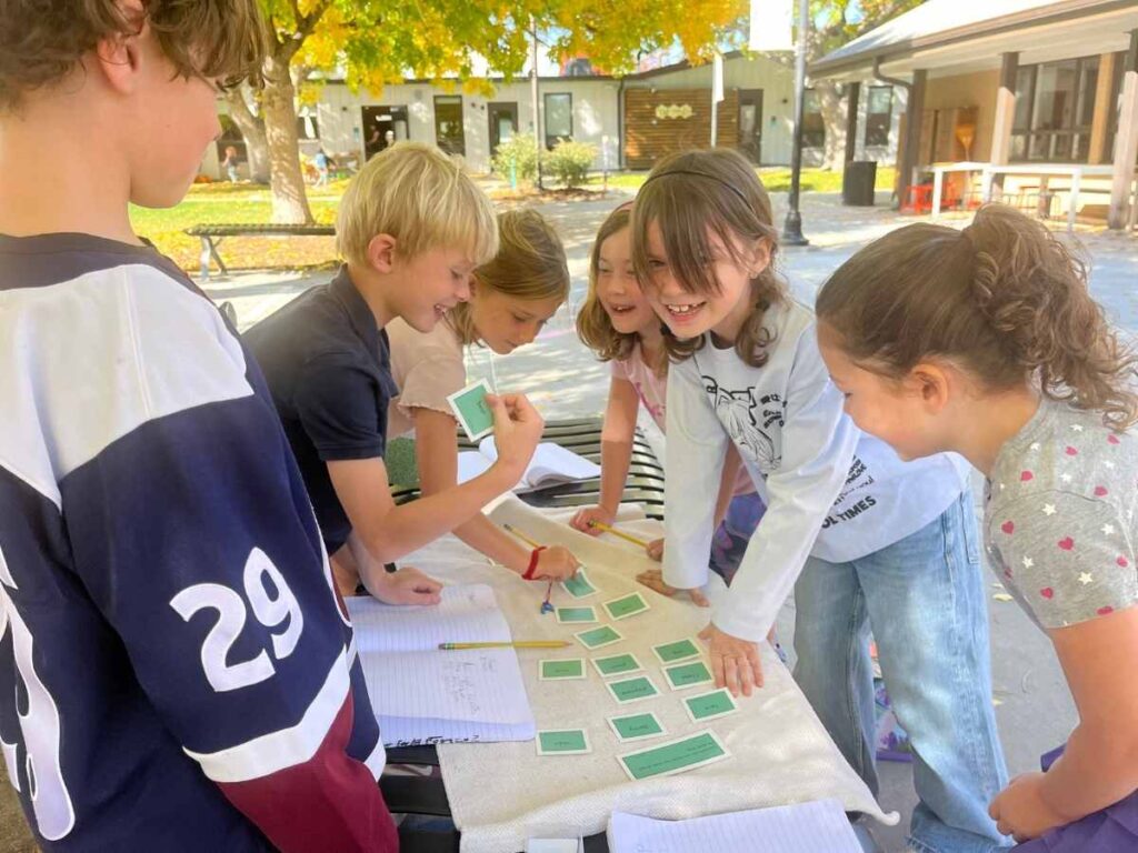 Kids outdoors around a table building confidence by working on hands on projects with each other for article The Joy Factor: How Montessori School of Denver Helps Kids Thrive for newcomers moving to Denver.