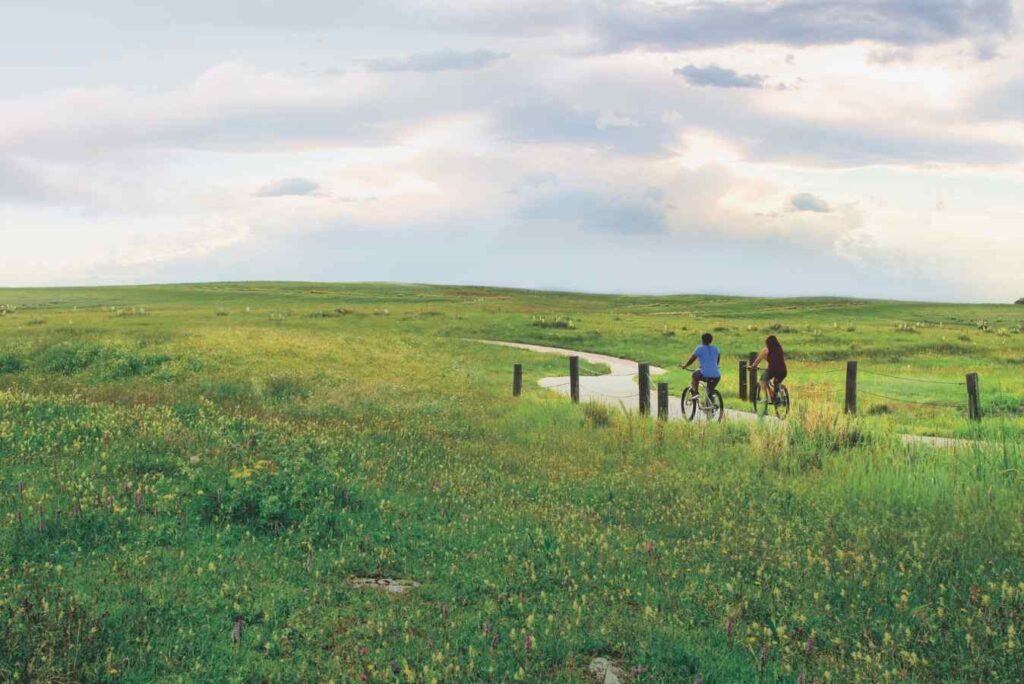 2 people riding their bicycles on Round Barn Trail through a wide open field for article Aurora, Colorado: The World in a City for newcomers moving to Denver or moving within Denver. 