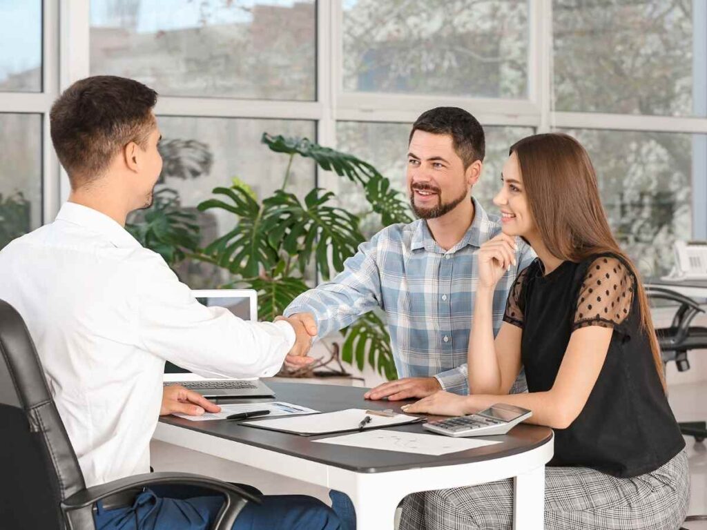 Couple sitting across desk from employee as the men shake hands over paperwork for article Credit Unions in Denver: A Newcomer’s Financial Playbook for newcomers moving to Denver Area.