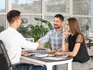 Couple sitting across desk from employee as the men shake hands over paperwork for article Credit Unions in Denver: A Newcomer’s Financial Playbook for newcomers moving to Denver Area.