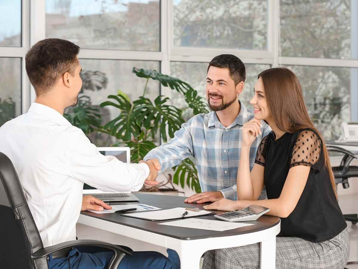 Couple sitting across desk from employee as the men shake hands over paperwork for article Credit Unions in Denver: A Newcomer’s Financial Playbook for newcomers moving to Denver Area.