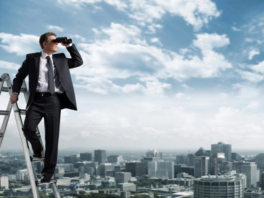 Picture of a man in a business suit standing on a ladder looking through binoculars out at a city skyline for article Top 10 Job Sites for a Successful Job Search in Denver for newcomers moving to Denver.
