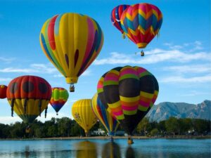 Hot air balloons on Lake Prospect in downtown Colorado Springs with mountains in the background for article Colorado Springs for newcomers moving to Denver area.