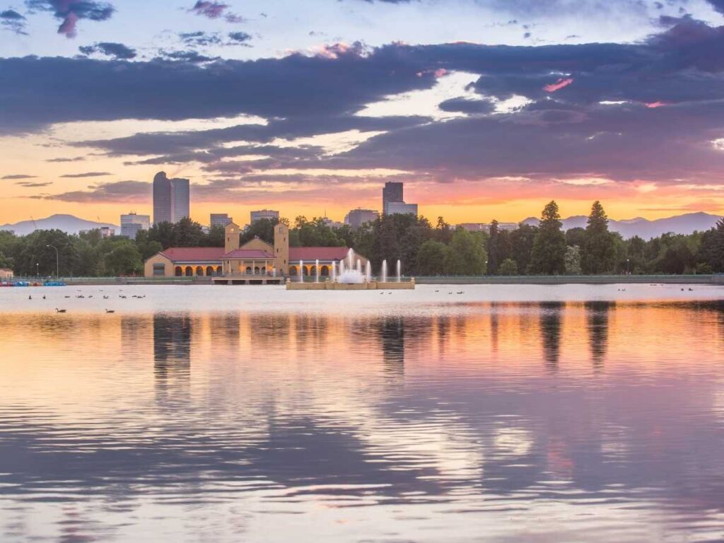 lake in the foreground in Denver park with downtown in the background and sun setting behind the mountains behind that for article Best Time of Year to Move to Denver: A Seasonal Guide for newcomers moving to Denver.