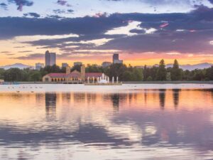 lake in the foreground in Denver park with downtown in the background and sun setting behind the mountains behind that for article Best Time of Year to Move to Denver: A Seasonal Guide for newcomers moving to Denver.