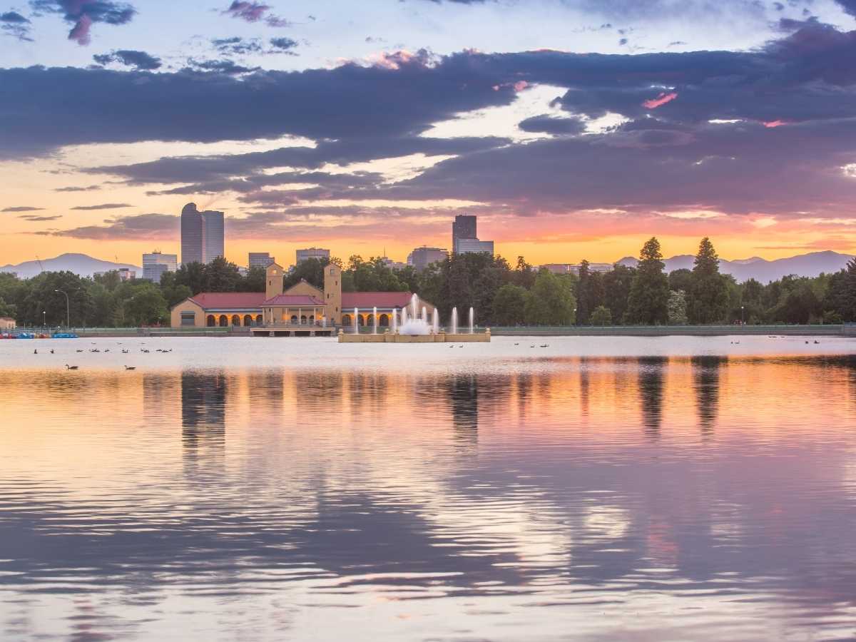 lake in the foreground in Denver park with downtown in the background and sun setting behind the mountains behind that for article Best Time of Year to Move to Denver: A Seasonal Guide for newcomers moving to Denver.