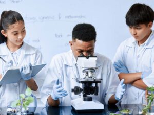 2 students in white lab coats on either side of teacher in lab coat looking into microscope in STEM class for article Denver Schools Guide: Public & Private Options (2025–2026) for newcomers moving to Denver area.